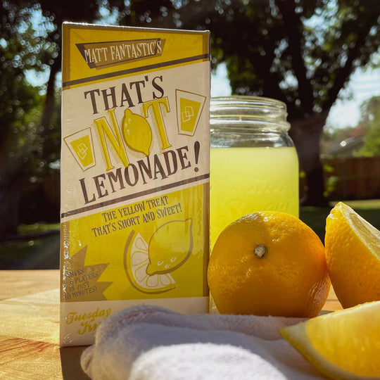 That's Not Lemonade bluffing game box on a table with a drink that looks like lemonade and lemons